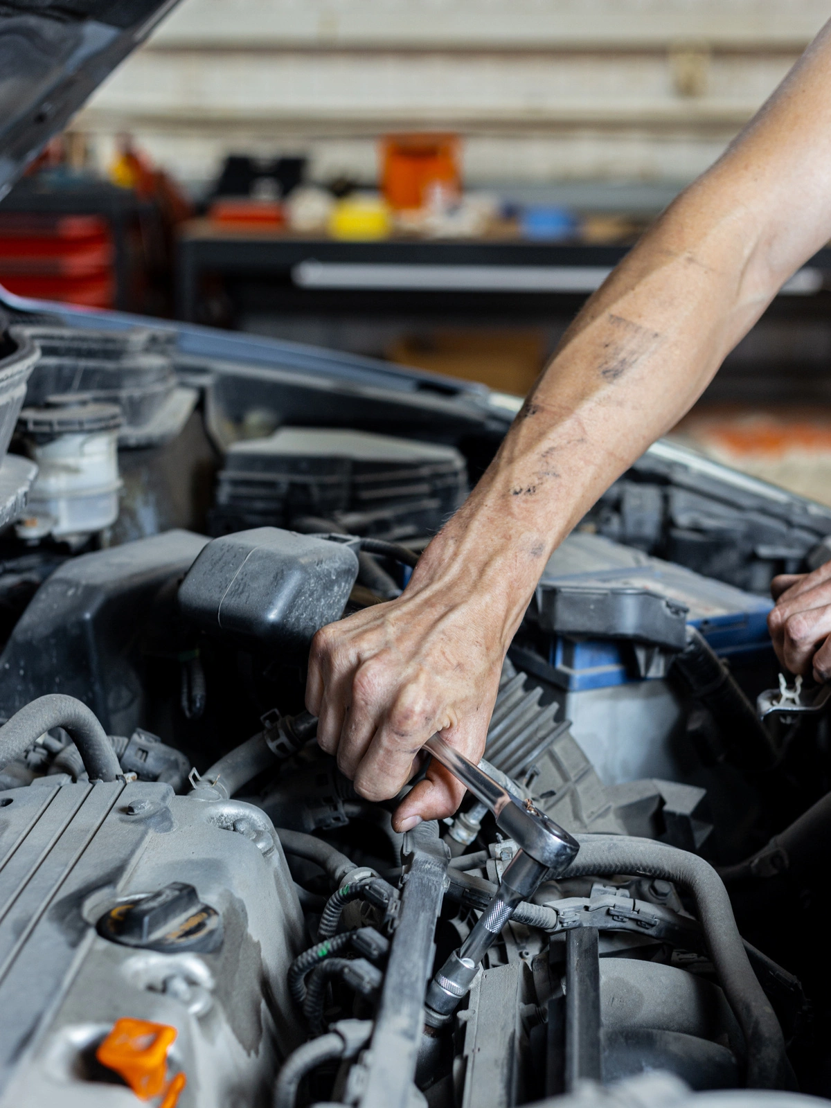 Mécanicien effectuant une réparation sur le moteur d'une voiture dans un atelier automobile, avec des outils à la main.